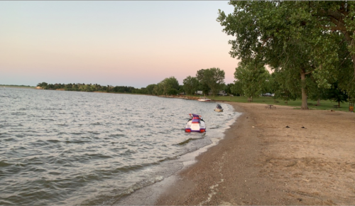 A serene beach at sunset with two jet skis on the water and trees lining the shore.