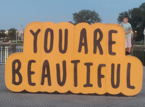 A large, colorful sign that reads "YOU ARE BEAUTIFUL," with a child standing nearby.