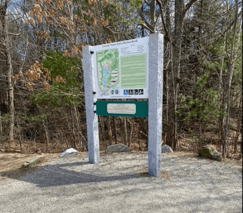 Trailhead sign for the Lawrence Nature Trail, featuring a map and information about the area, surrounded by trees.