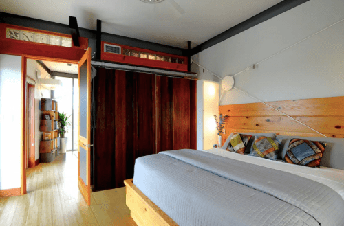 Modern bedroom with wooden accents, a large bed, and an open doorway leading to a bright hallway.