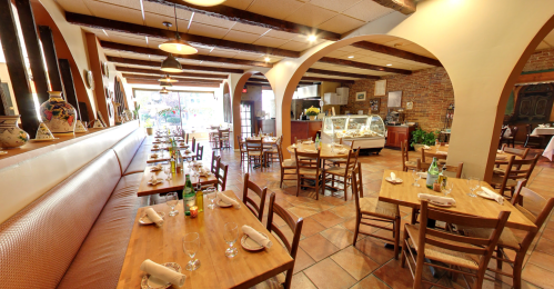 Cozy restaurant interior with wooden tables, chairs, and a display case, featuring warm lighting and brick walls.