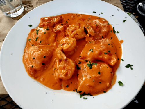 A plate of ravioli and shrimp in a creamy orange sauce, garnished with parsley.