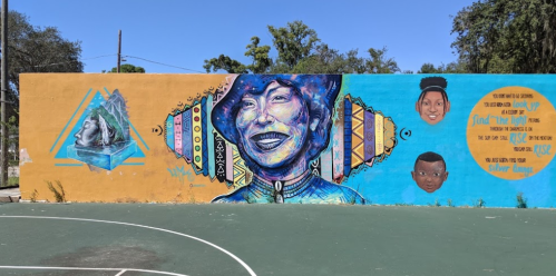 Colorful mural featuring a smiling woman, geometric patterns, and portraits of two children on a basketball court wall.