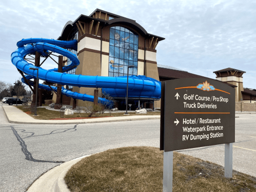 A blue water slide spirals down from a building with a sign for a golf course, hotel, and waterpark entrance.