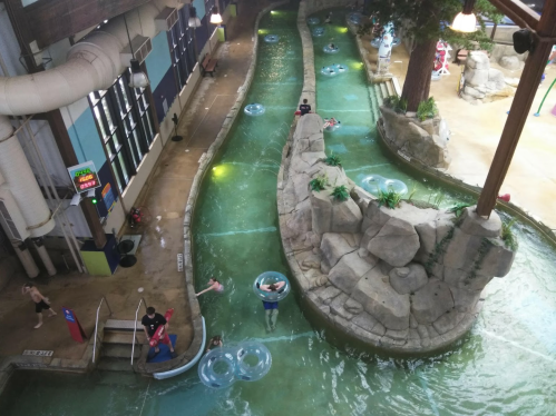 Aerial view of a water park's lazy river with rocks, greenery, and people floating on tubes.