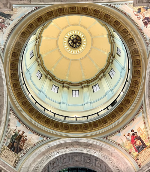 A view of a circular dome with intricate designs and murals, showcasing architectural details from below.