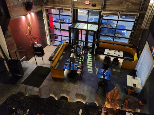 Aerial view of a modern restaurant with a bar, seating areas, and a large mural on the wall.