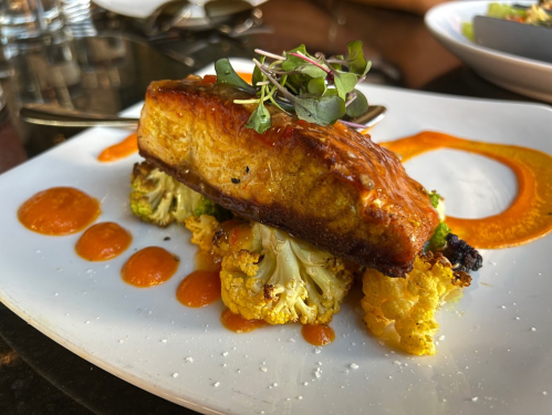 A beautifully plated dish featuring a piece of seared tofu on roasted cauliflower with a drizzle of sauce and microgreens.