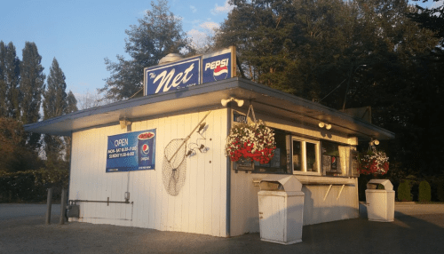 A small food kiosk named "The Net," featuring a Pepsi sign and flower baskets, surrounded by trees.