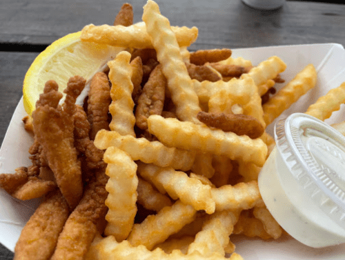 A serving of crinkle-cut fries with a lemon wedge and a small cup of dipping sauce.