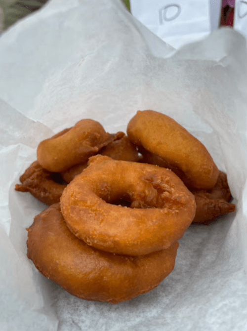 A small pile of golden-brown, freshly fried donuts on a piece of white parchment paper.