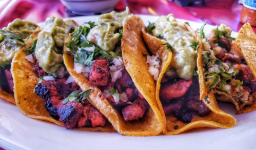 A plate of tacos filled with grilled meat, topped with onions, cilantro, and guacamole.