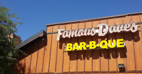 Sign for Famous Dave's Bar-B-Que on a wooden building with a clear blue sky above.