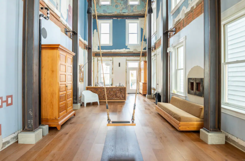 A spacious interior with high ceilings, wooden floors, a swing, and large windows, featuring artistic wall designs.
