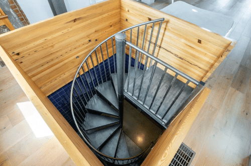 A spiral staircase with a metal railing, surrounded by wooden walls and blue tiles, viewed from above.