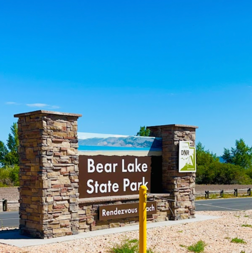Sign for Bear Lake State Park at Rendezvous Beach, featuring stone pillars and a clear blue sky.