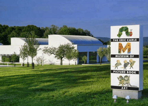 Exterior of the Eric Carle Museum of Picture Book Art, featuring a sign and green landscape under a clear blue sky.