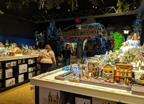 A festive display of miniature holiday villages and decorations, with shoppers exploring a warmly lit store.