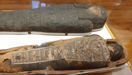 Two ancient Egyptian sarcophagi displayed in a museum, showcasing intricate carvings and hieroglyphics.