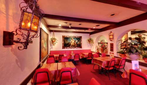 Cozy restaurant interior with red chairs, tables, and decorative wall art, featuring warm lighting and plants.