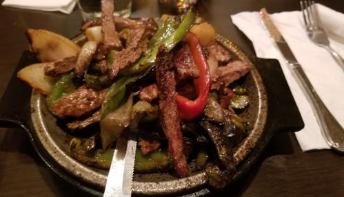 Sizzling platter of grilled steak, bell peppers, and onions served on a hot stone.