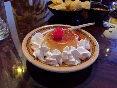 A creamy dessert topped with a cherry and surrounded by whipped cream, served on a decorative plate.