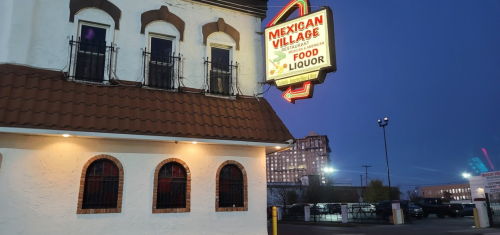 Exterior of Mexican Village restaurant at dusk, featuring a neon sign and distinctive architectural details.