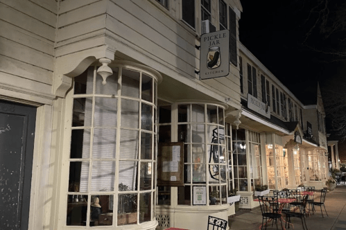 Exterior of a restaurant called "Pickle Jar Kitchen," featuring large windows and outdoor seating at night.