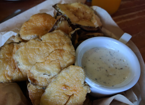 A basket of crispy fried vegetables served with a small bowl of creamy dipping sauce.