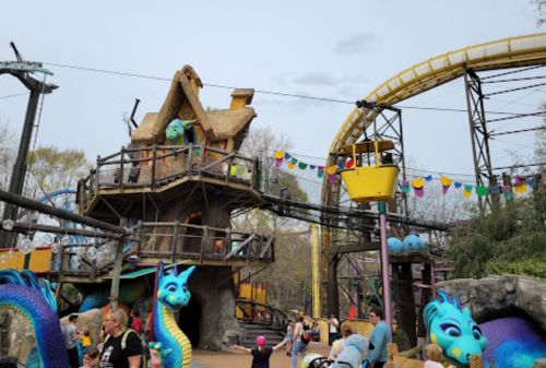 A whimsical amusement park scene featuring a colorful ride, a dragon statue, and a treehouse structure.