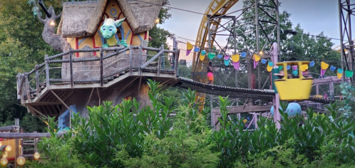 A whimsical treehouse with colorful decorations and a roller coaster in the background, surrounded by greenery.