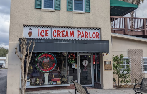 A colorful ice cream parlor with a sign reading "Ice Cream Parlor" and an open neon sign in the window.