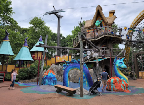 Colorful play area with whimsical structures, including a treehouse and dragon sculptures, surrounded by greenery.