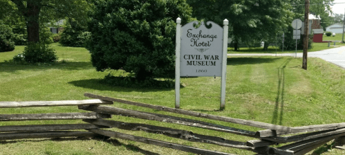 Sign for the Exchange Hotel Civil War Museum, surrounded by greenery and a wooden fence.
