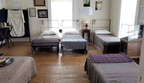 A historic bedroom with four beds, simple decor, and a lamp, showcasing a museum exhibit on past living conditions.
