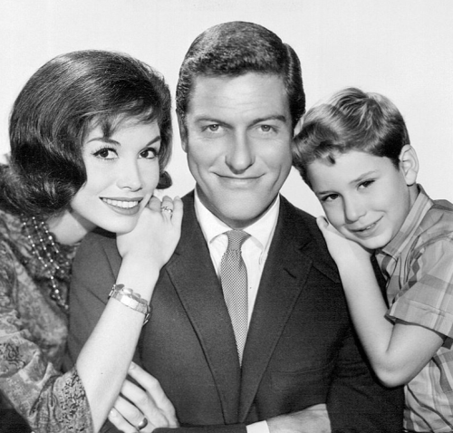 A black-and-white photo of a smiling woman, man, and boy posing closely together, showcasing a warm family moment.