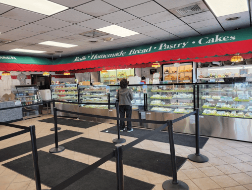 A bakery interior with display cases filled with pastries and a customer browsing the selection.