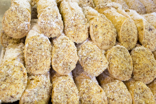A close-up of stacked pastries coated in powdered sugar and nuts, showcasing their golden-brown texture.