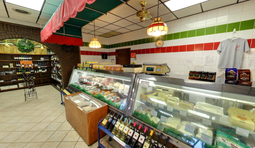 A cozy deli with a glass display of cheeses, wines, and colorful wall tiles in green, red, and white.
