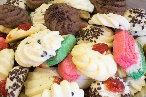 A colorful assortment of cookies, including chocolate, vanilla, and festive red and green varieties, topped with sprinkles and jam.