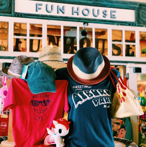 A display of colorful hats and shirts at a shop called "Fun House," with a plush toy in front.