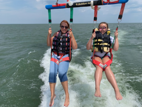 Two people in life vests enjoying parasailing over the ocean, with waves splashing below them.