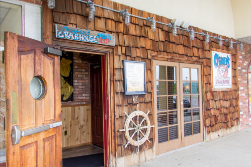 Exterior of a crab house with wooden shingles, a ship's wheel, and a welcoming entrance.