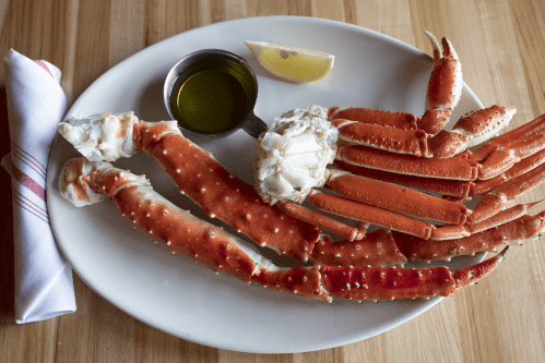 A plate of crab legs with a lemon wedge and a small bowl of dipping sauce, set on a wooden table.