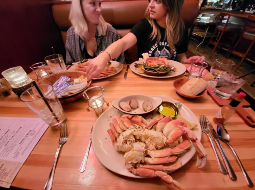Two women at a restaurant table enjoying a seafood meal with crab, sides, and drinks.