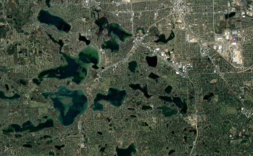 Aerial view of a landscape featuring multiple lakes, urban areas, and green spaces.
