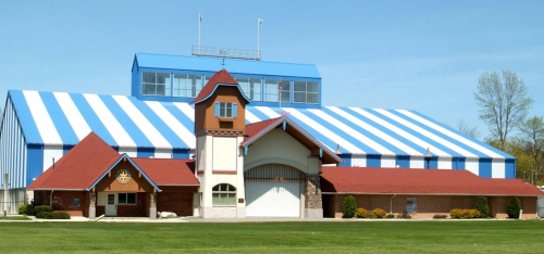 A large building with a blue and white striped roof, featuring a brick entrance and a clock tower. Green lawn in front.