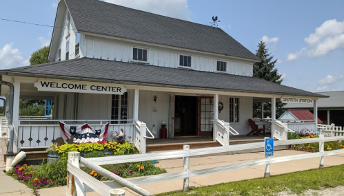 A white building with a sign reading "Welcome Center" and colorful flowers in front, set against a blue sky.