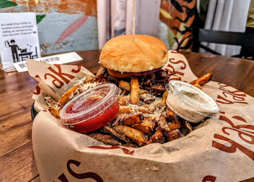 A basket of fries topped with meat, a sandwich, and two dipping sauces on a wooden table.