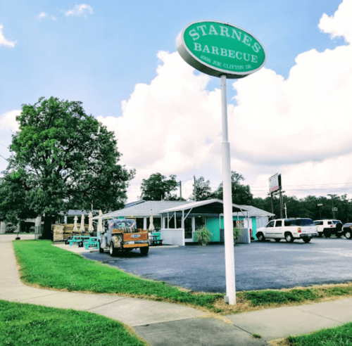 A barbecue restaurant with a sign reading "Starnes Barbecue," featuring outdoor seating and parked vehicles.